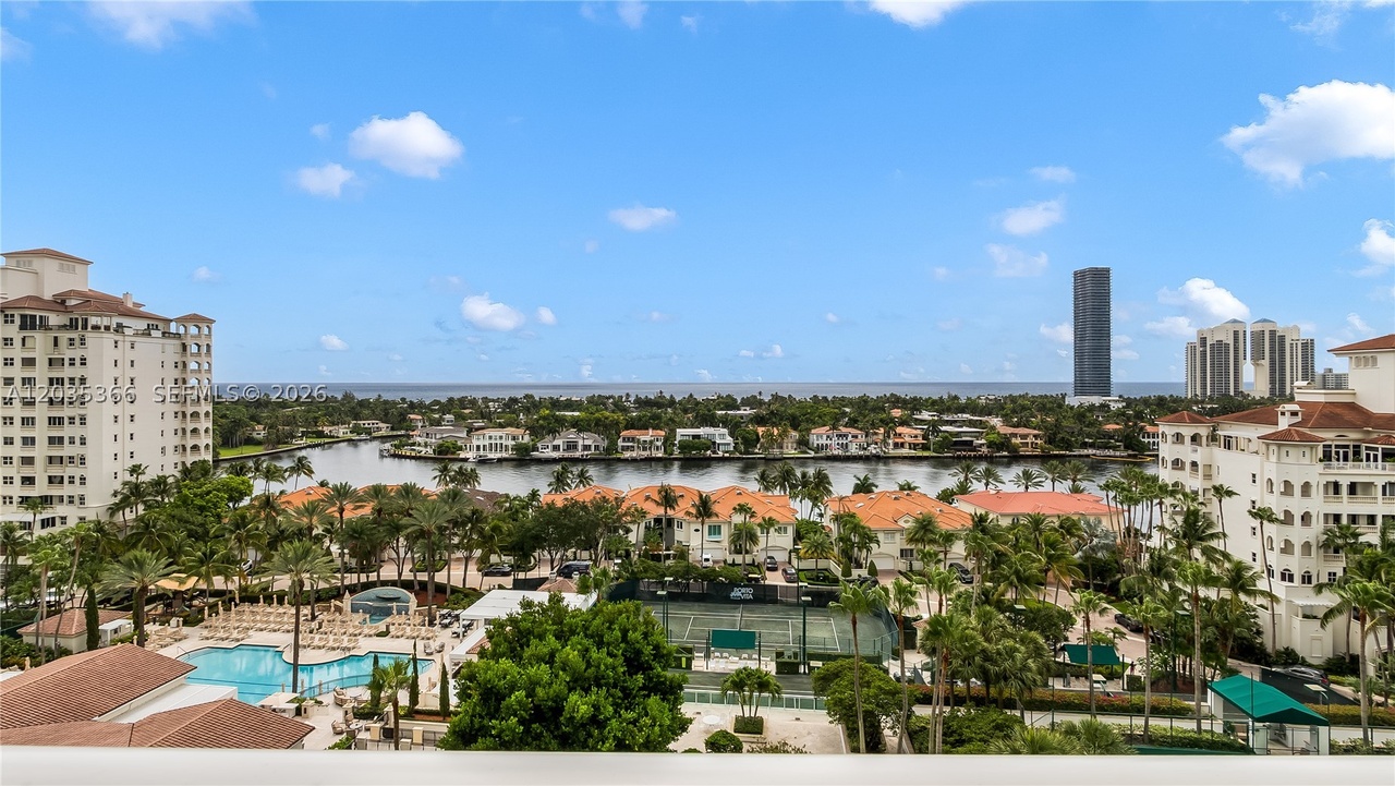 Panoramic view from the Residence 1205 terrace over the Intracoastal Waterway to the Atlantic on the horizon, with the resort pool and tennis courts below and palm-lined waterfront homes across the water