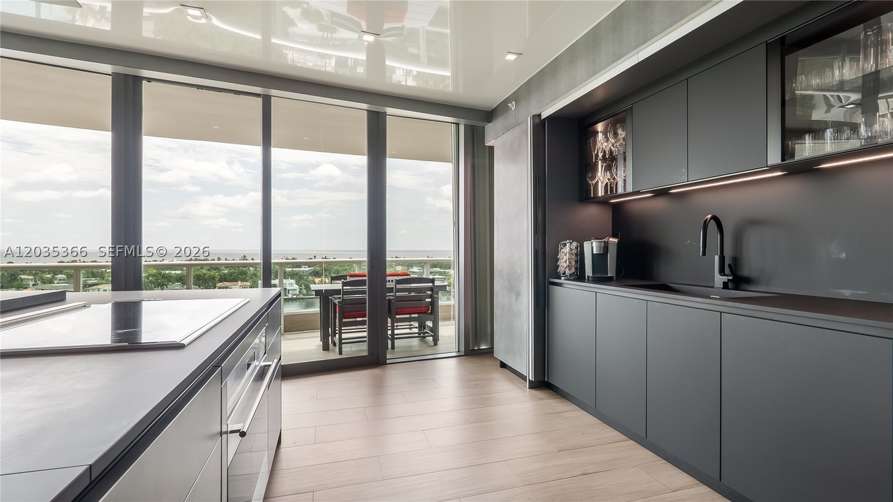 The kitchen looking toward the dining table on the terrace, with sliding glass doors open to the water view and a charcoal galley along the right wall