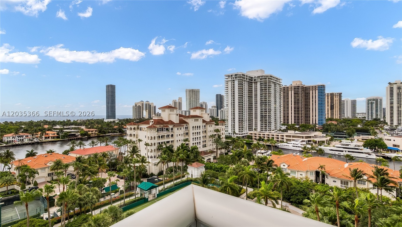 A high aerial over the Intracoastal showing the marina, the Sunny Isles high-rises, red-roofed waterfront villas, and the ocean beyond under a blue sky
