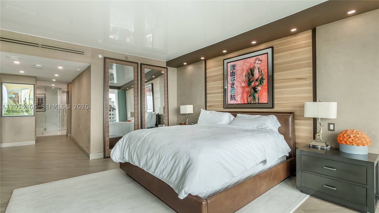The primary bedroom with a leather platform bed, a wood-paneled headboard wall, a framed James Dean poster, paired full-length mirrors, and the reflective ceiling above