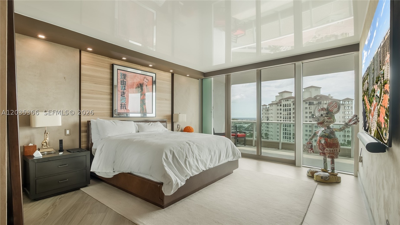 The second bedroom with sliding glass doors onto the terrace, a wall-mounted screen, a mixed-media sculpture, and the Intracoastal and skyline beyond
